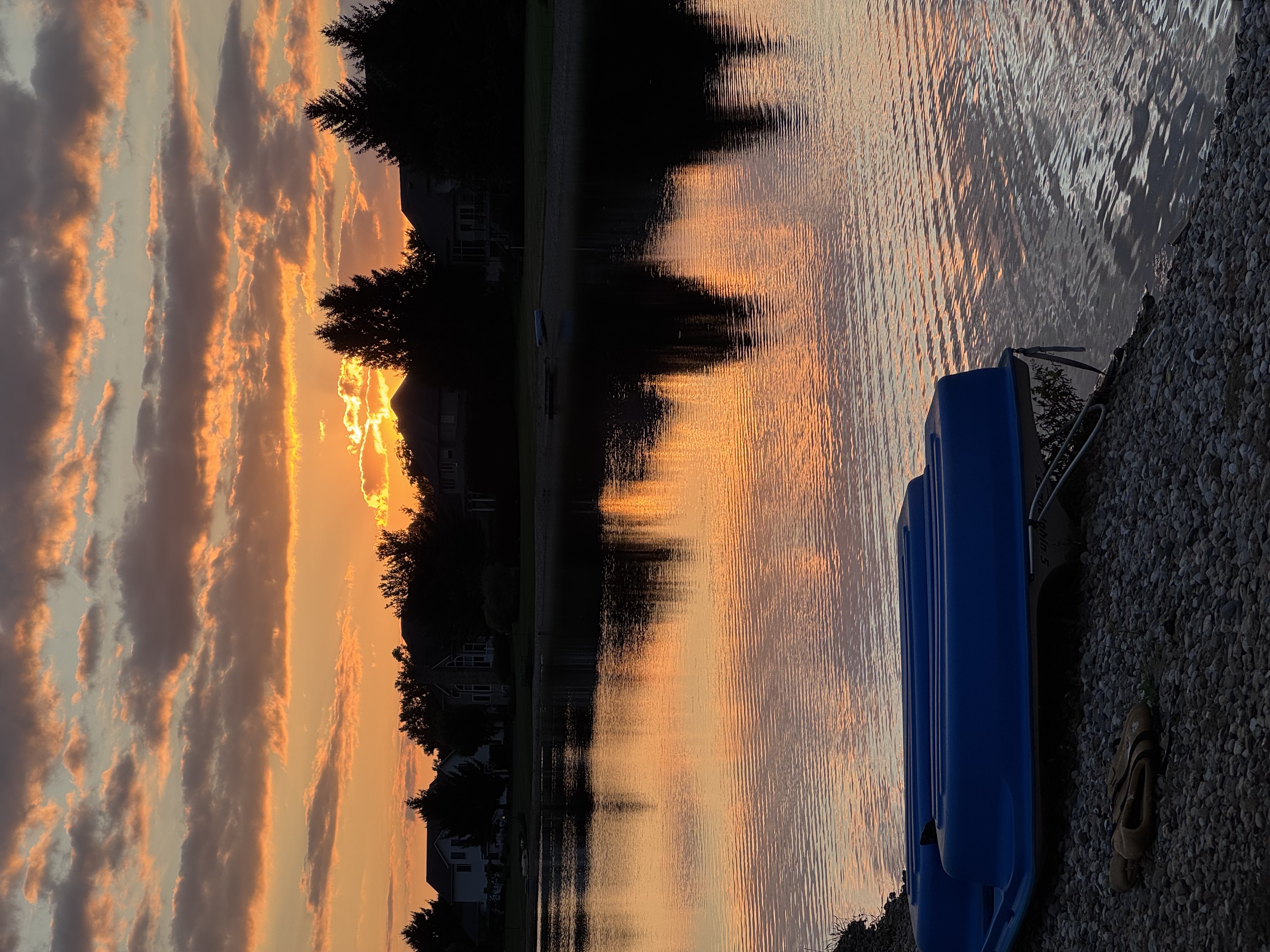 An orange sunset reflects in a lake behind blue boats on the shore.