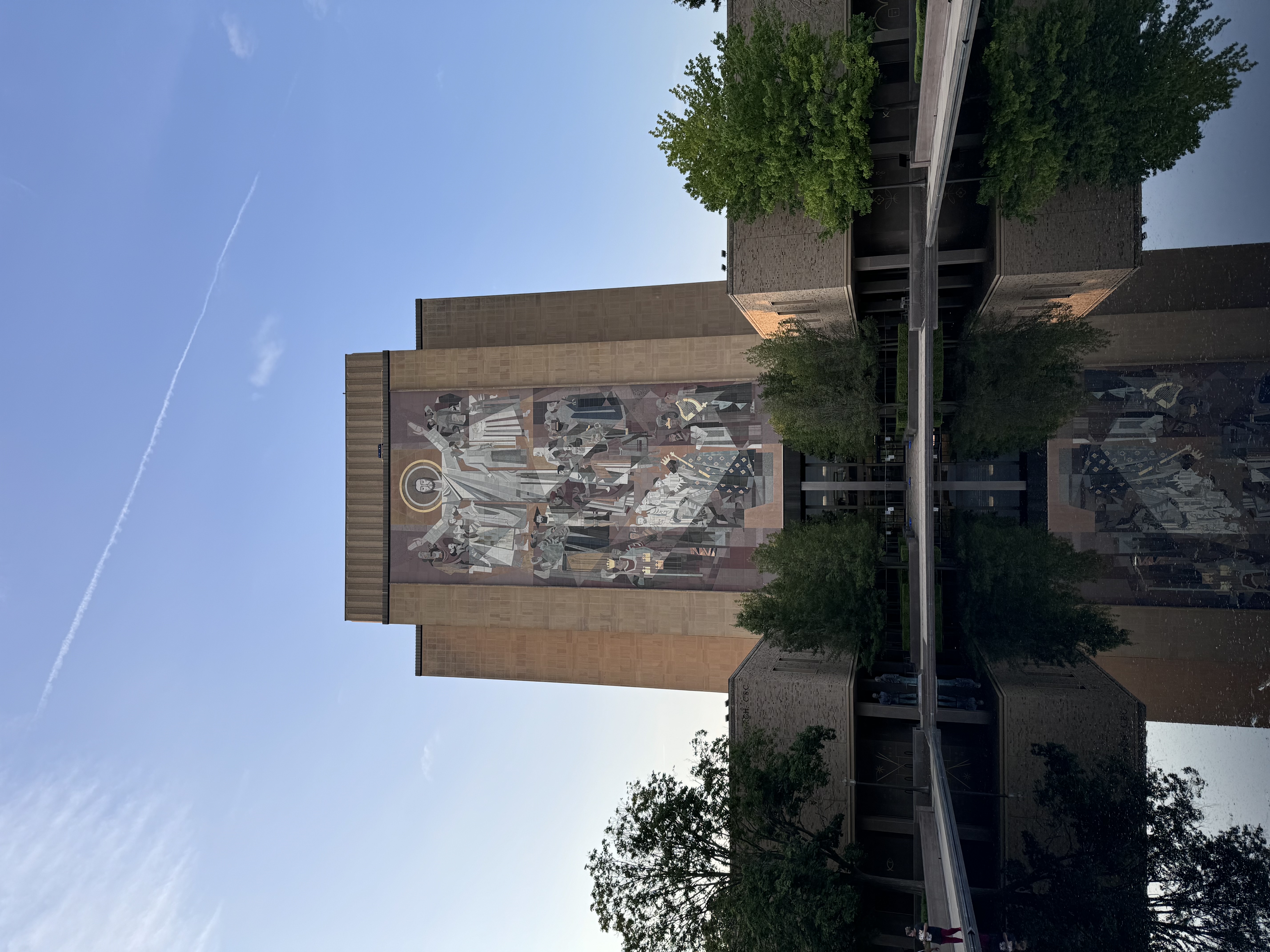 A monumental mural and its building reflected in a still pool.