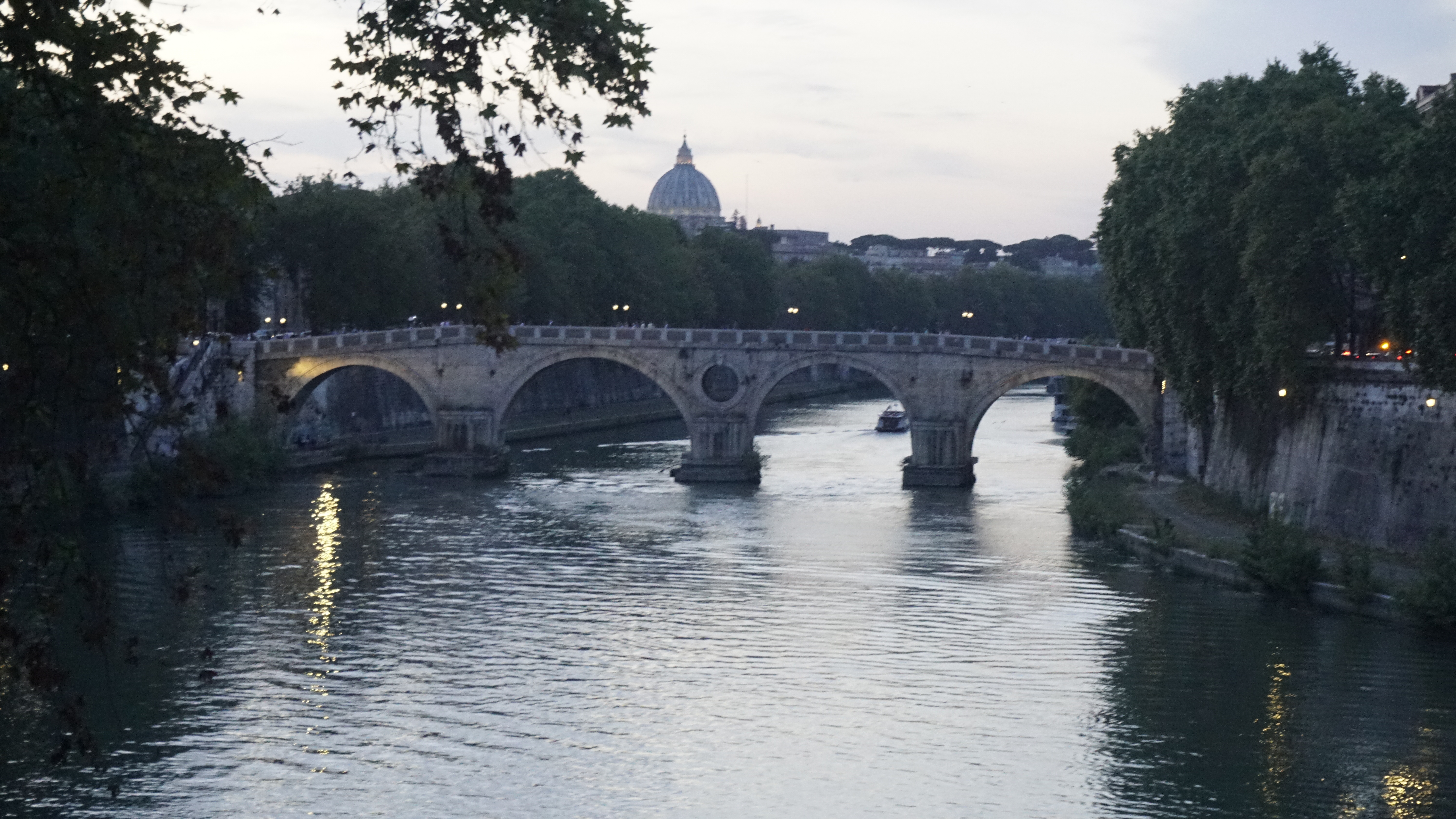 An arched stone bridge crosses a river beneath a distant dome.