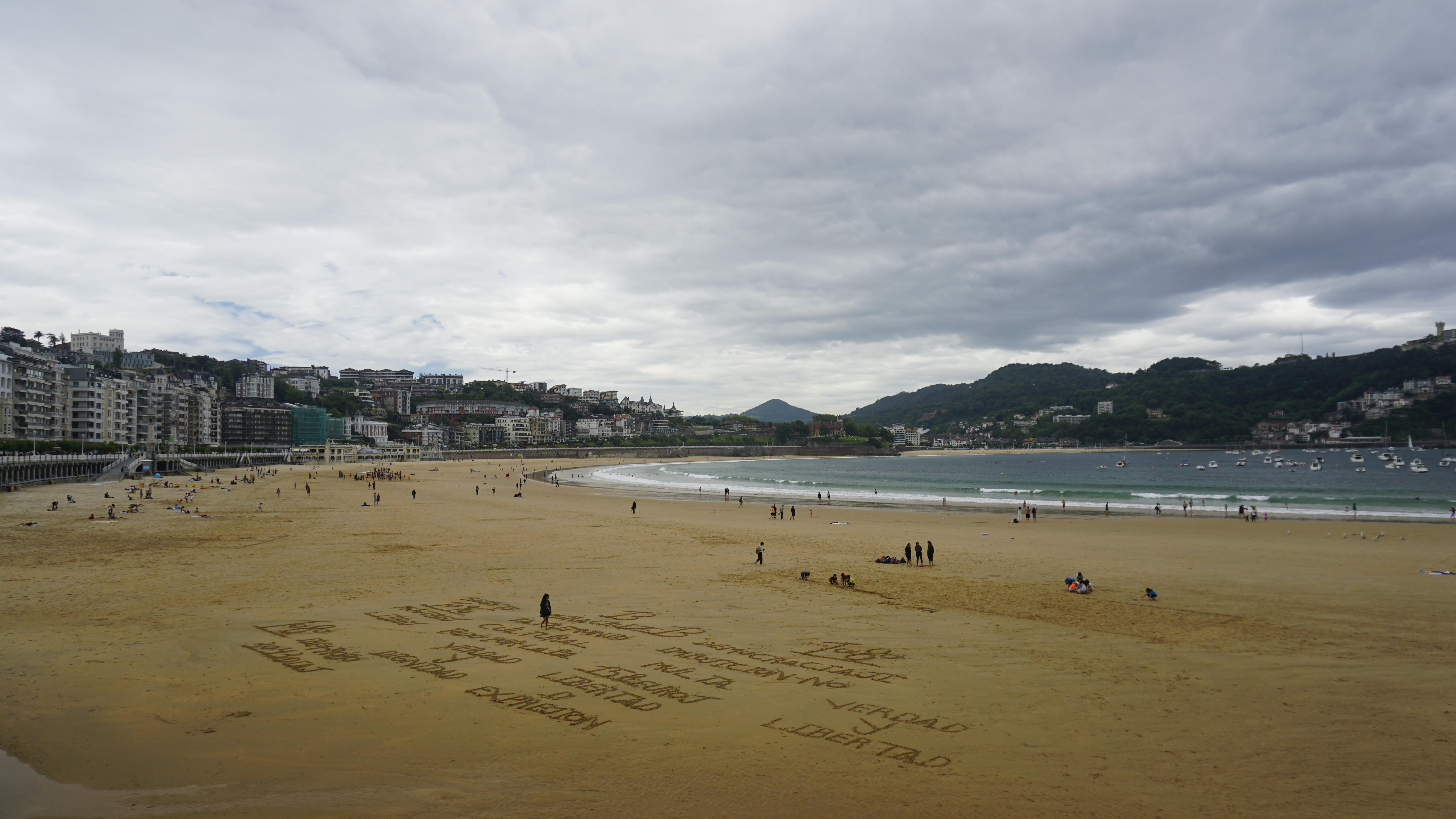 A broad beach with scattered people beneath an overcast sky.