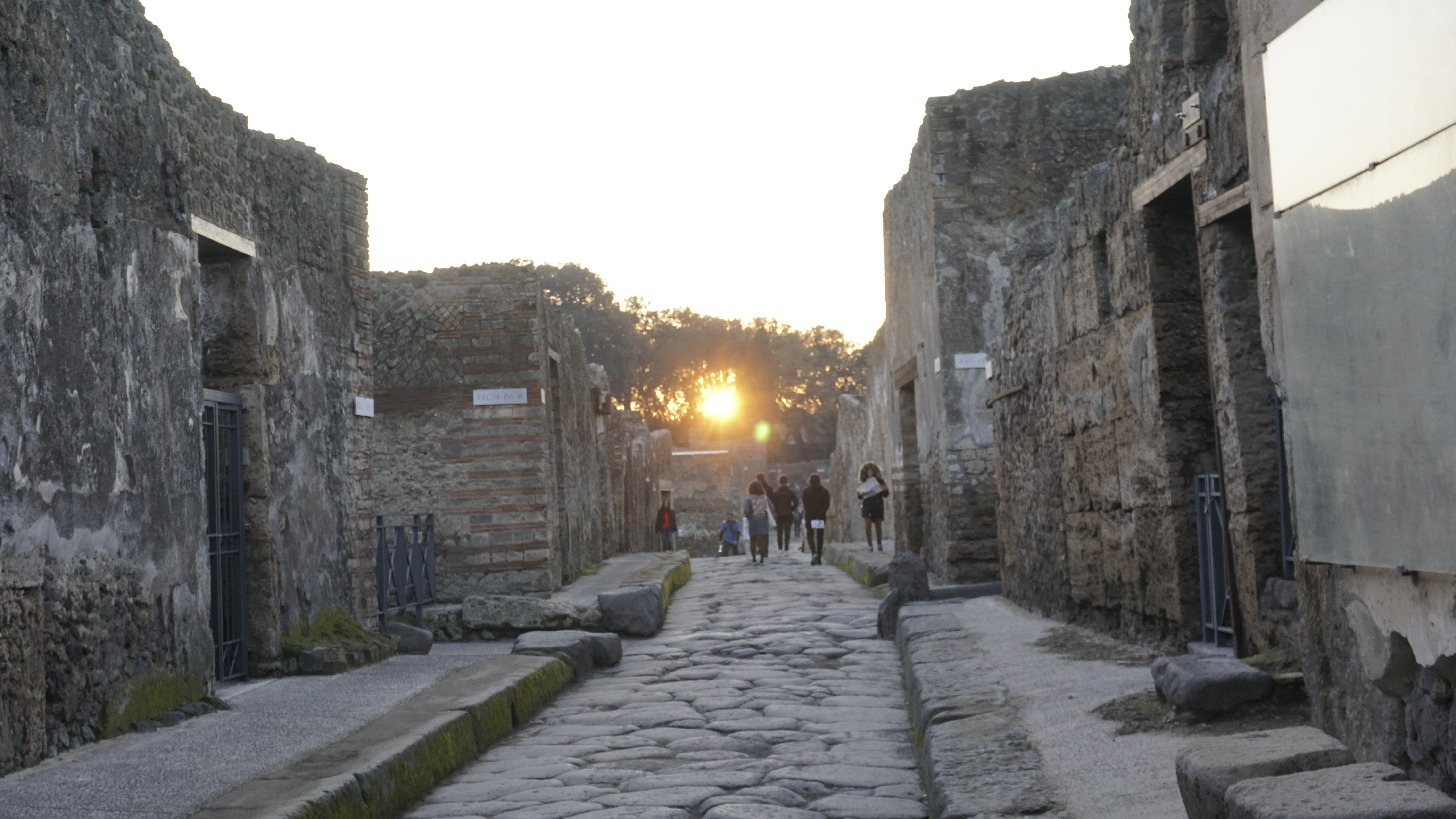 Low sunlight falls along an ancient stone street with distant walkers.