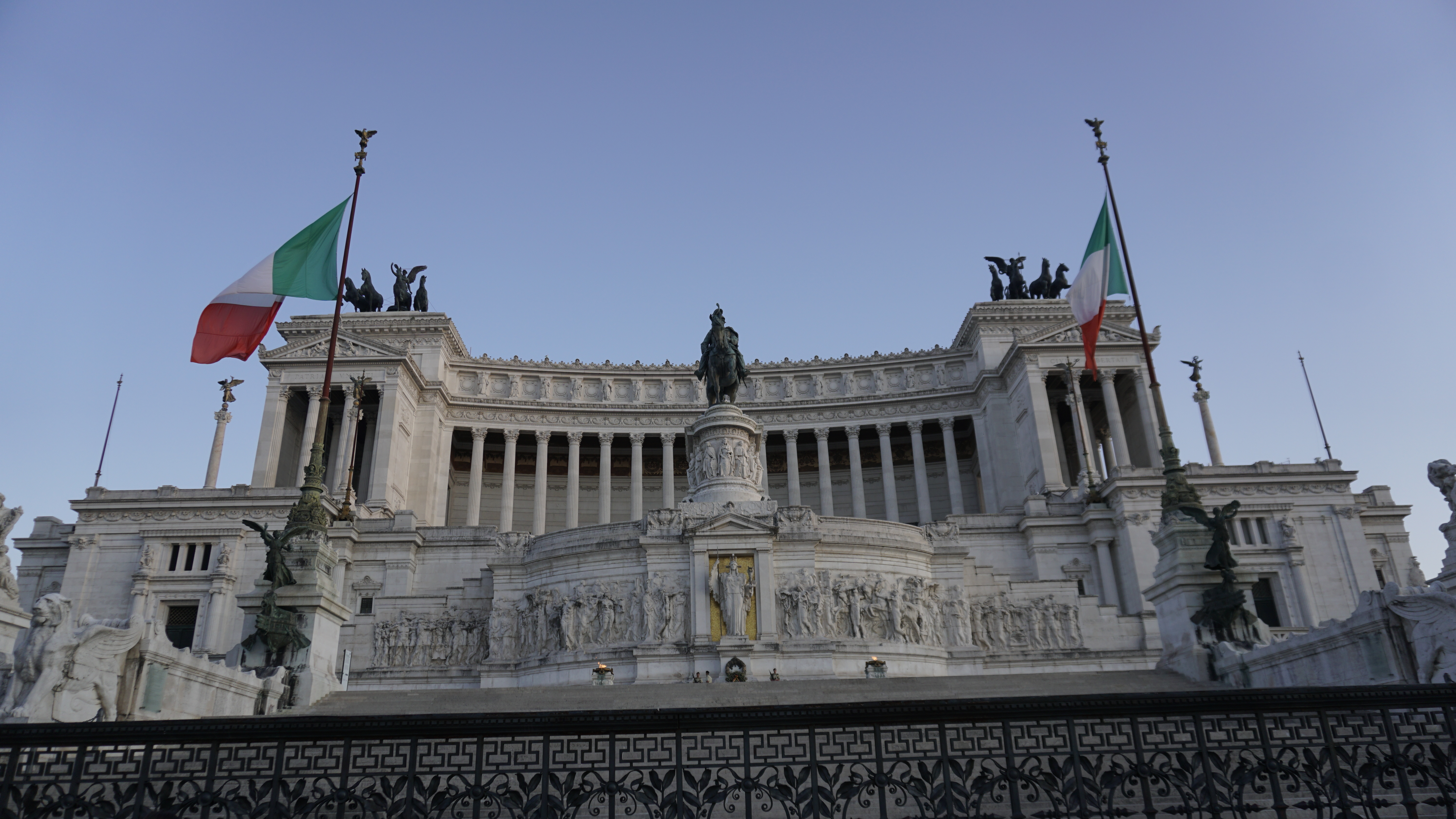 A white marble monument framed by two Italian flags.